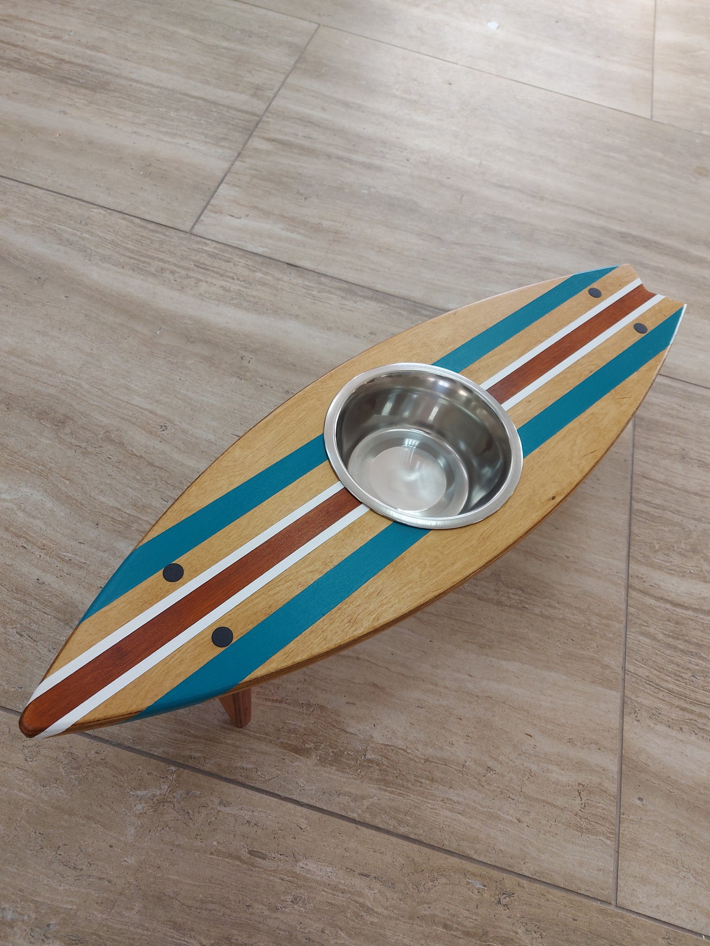 Colorful surfboard-shaped pet feeder with a metal bowl on a wooden floor.