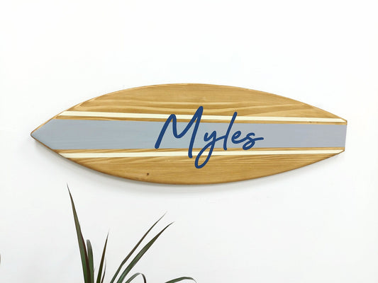 Coastal-themed wooden name sign in surfboard shape on wall