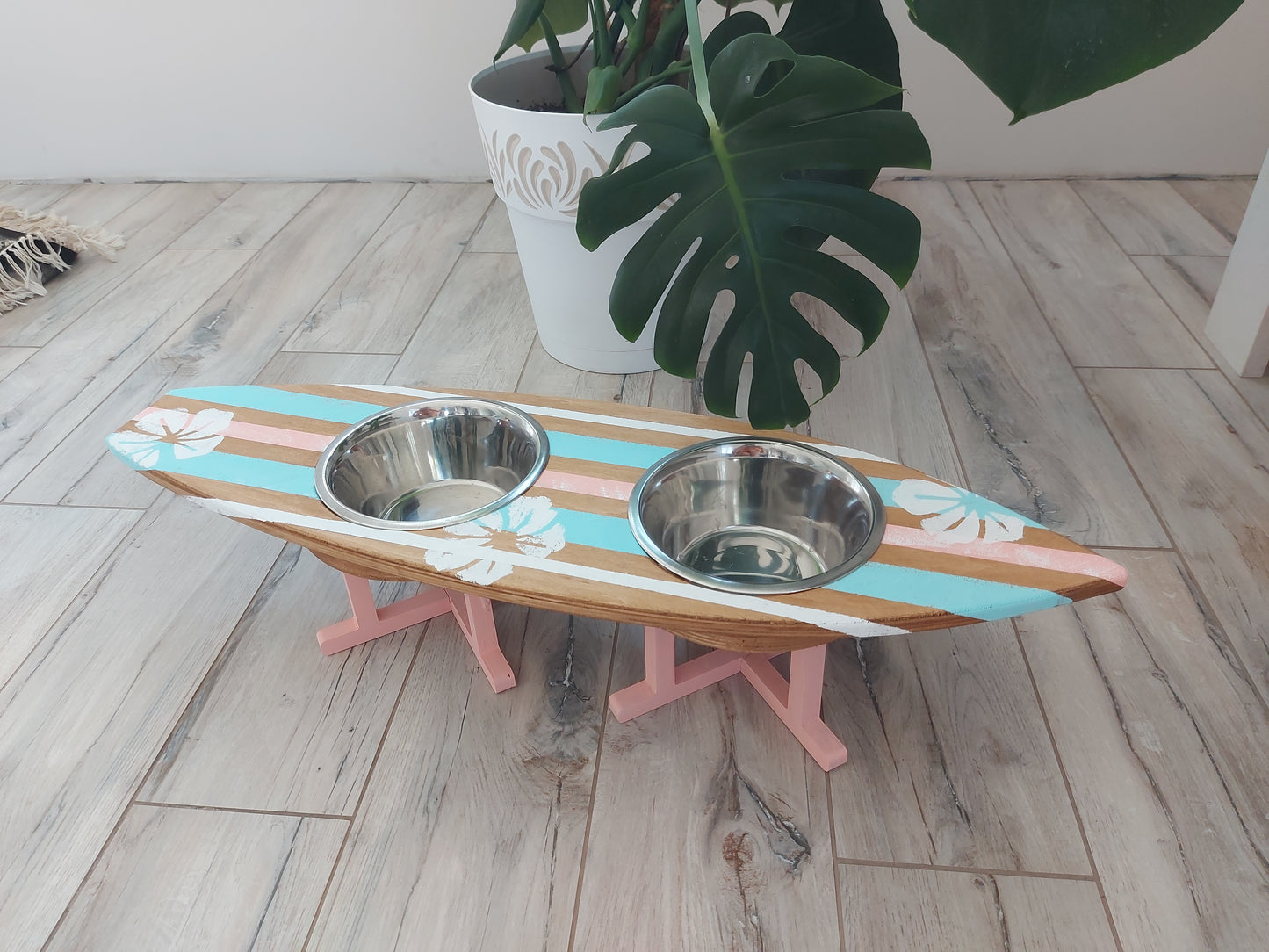 Pet bowl stand made in surfboard design with two metal bowls on a wooden floor.