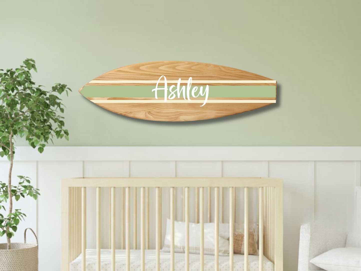 Wooden surfboard nameplate with 'Ashley' on a wall above a crib in a nursery.