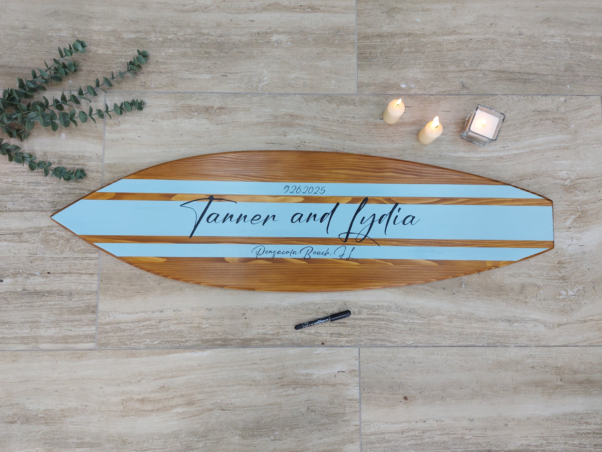 Wooden surfboard with blue stripe and engraved text on a wooden surface as a wedding sign guest book