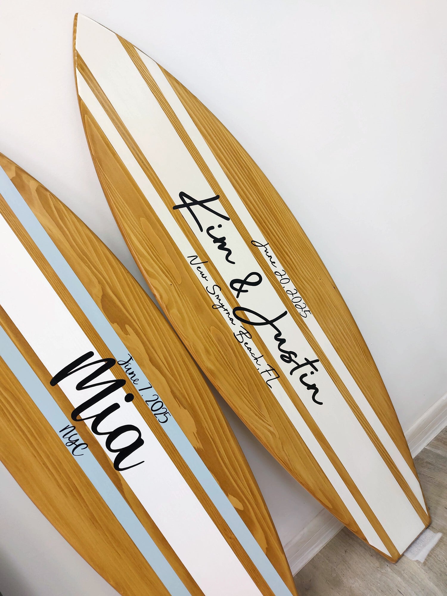 Two wooden surfboards wedding signs with names and dates engraved on a white background