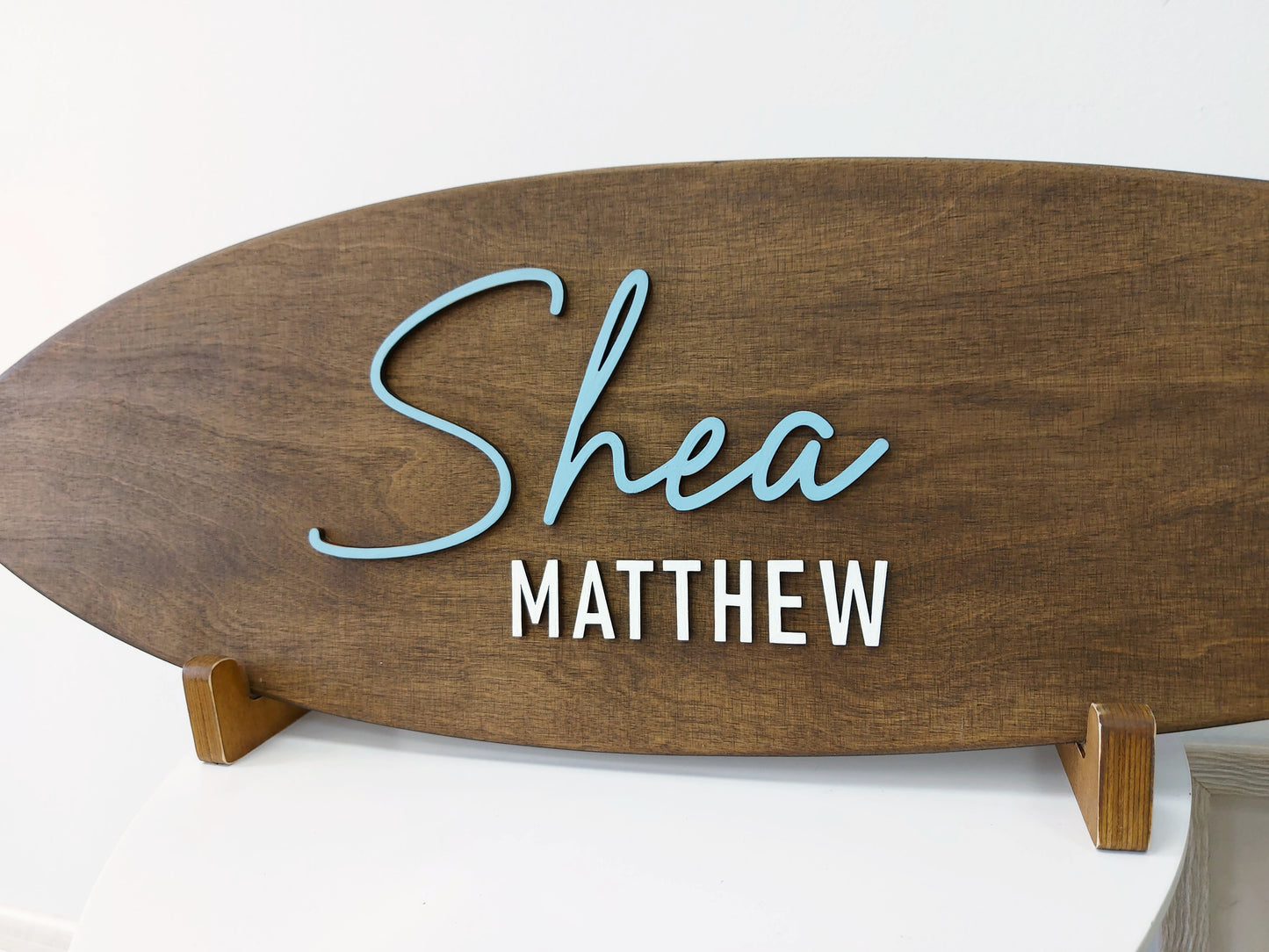 Close-up of custom wooden surfboard name plaque above baby crib
