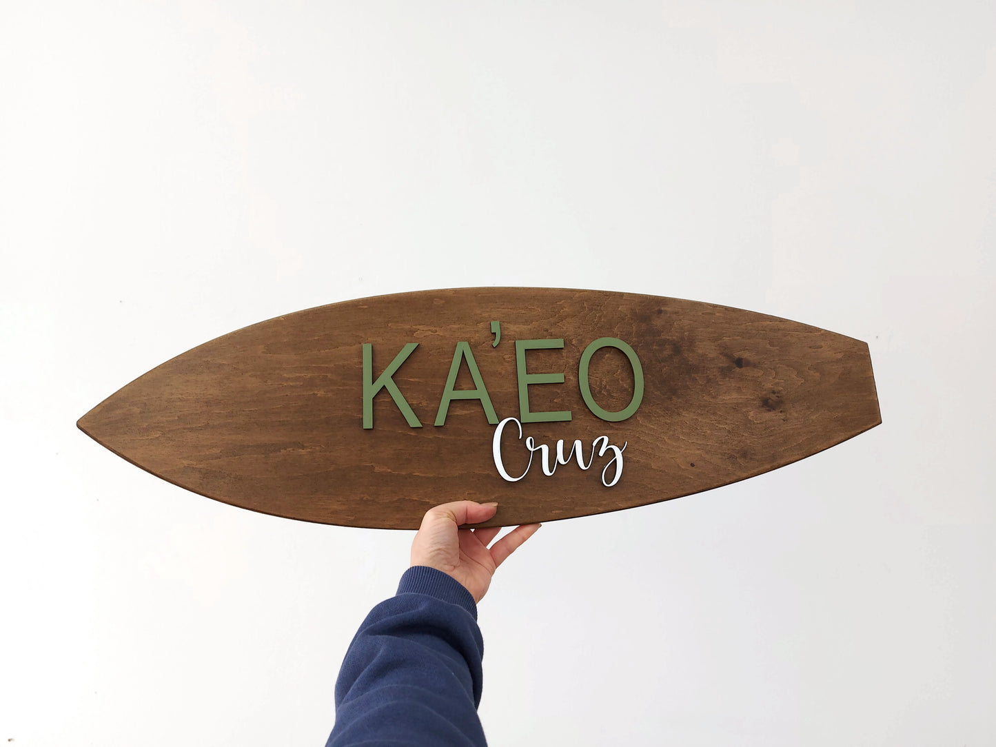 Wooden surfboard-shaped nursery sign with 'KA'EO Cruz' text on a white background
