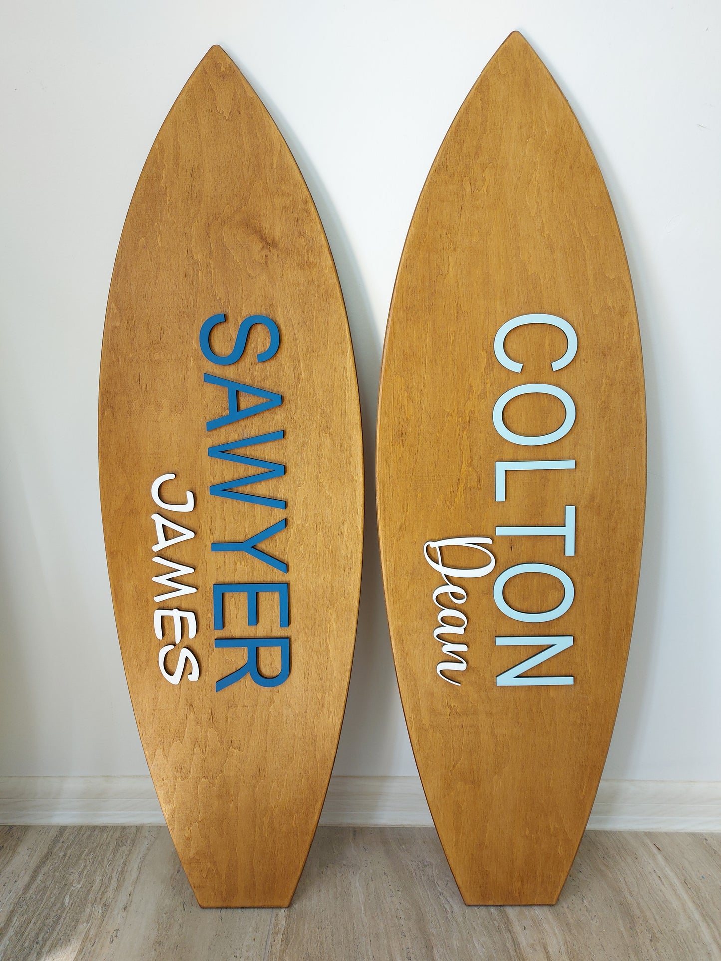 Two wooden surfboard nameplates with engraved names on a white wall.
