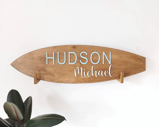 Personalized baby name surfboard sign hanging in coastal-style nursery