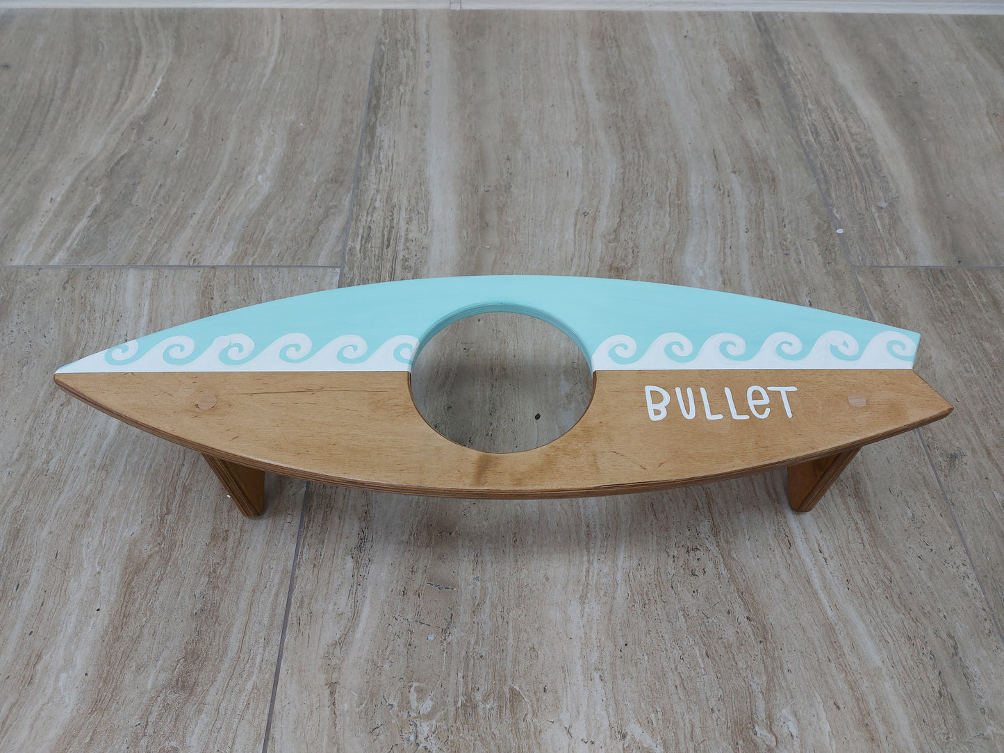 Personalized wooden surfboard bowl holder placed on floor with dog food