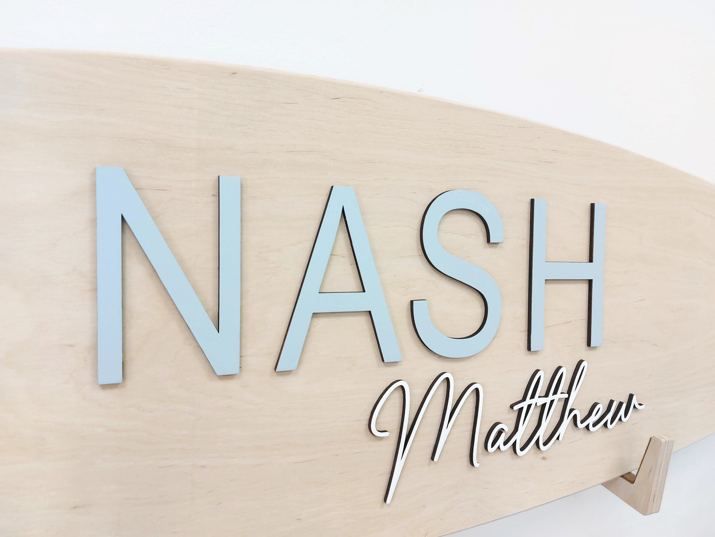 Wooden surfboard nameplate with 'NASH Matthew' engraved on a white background