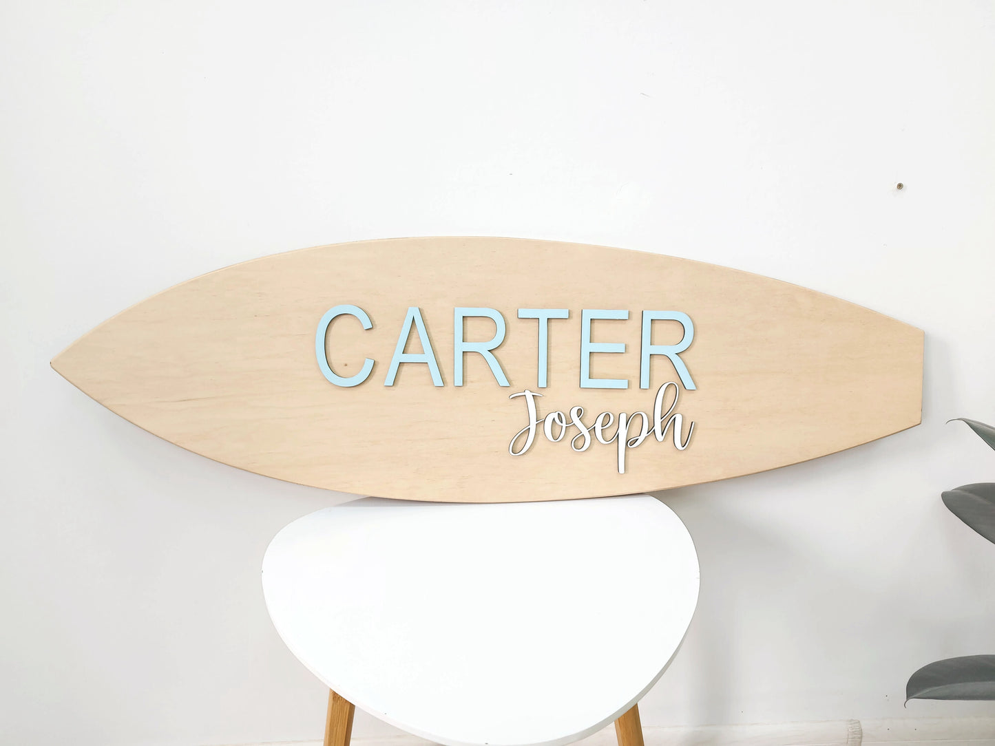 Wooden surfboard-shaped nameplate sign with 'Carter Joseph' engraved on a white background