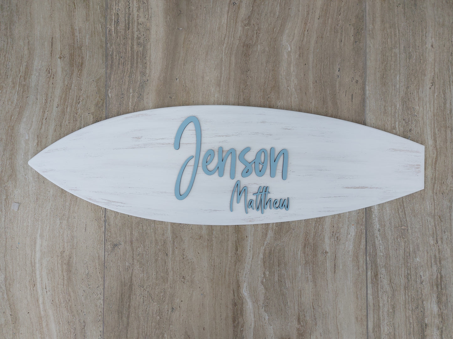 Wooden baby name sign shaped like a surfboard on pastel nursery wall