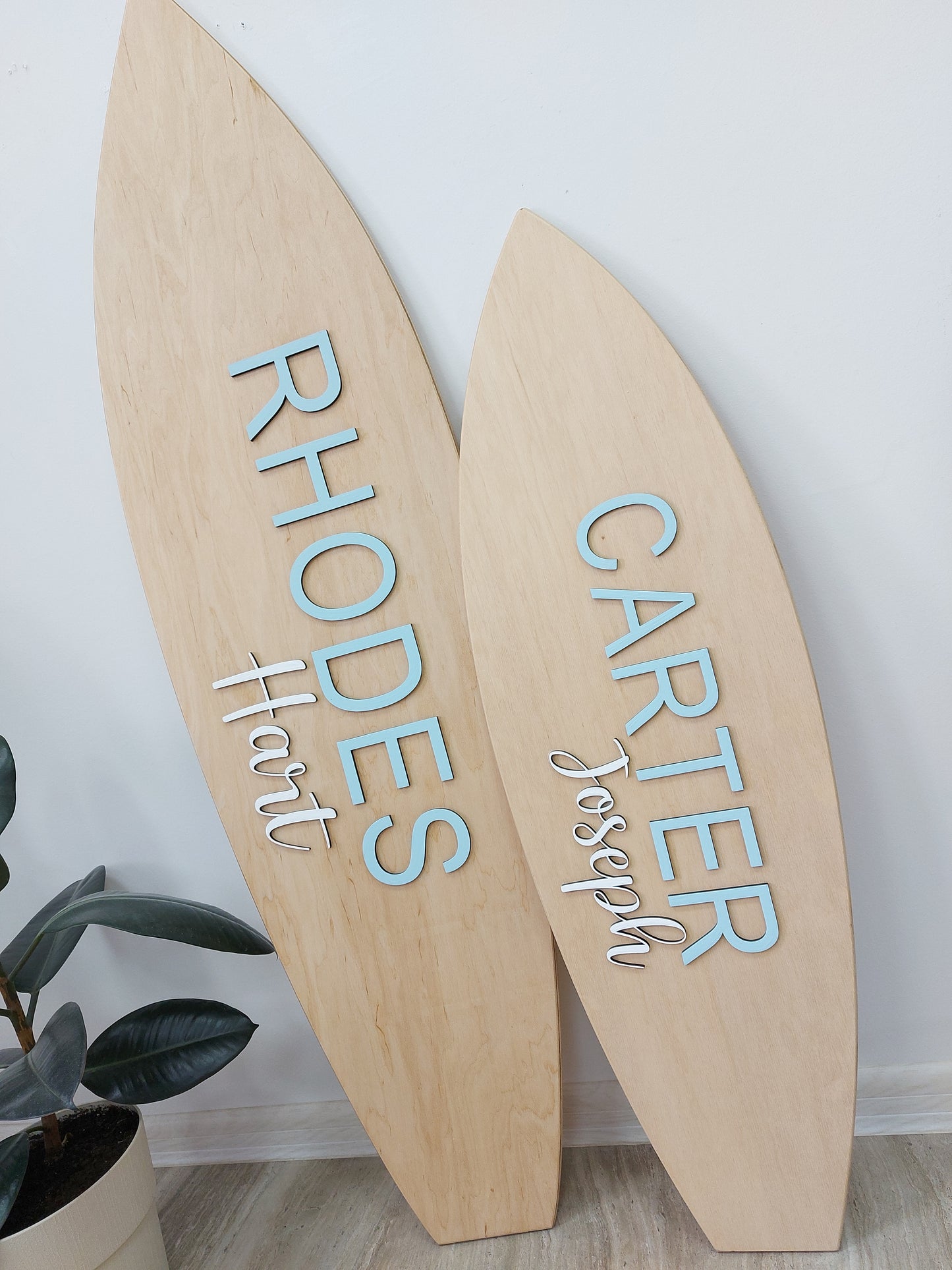 Wooden surfboard nameplates with engraved names on a white wall.
