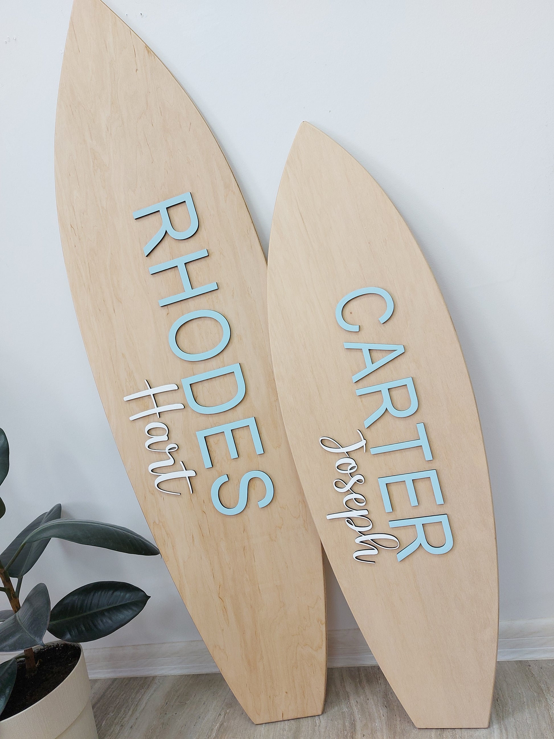 Wooden surfboard nameplates with engraved names on a white wall.