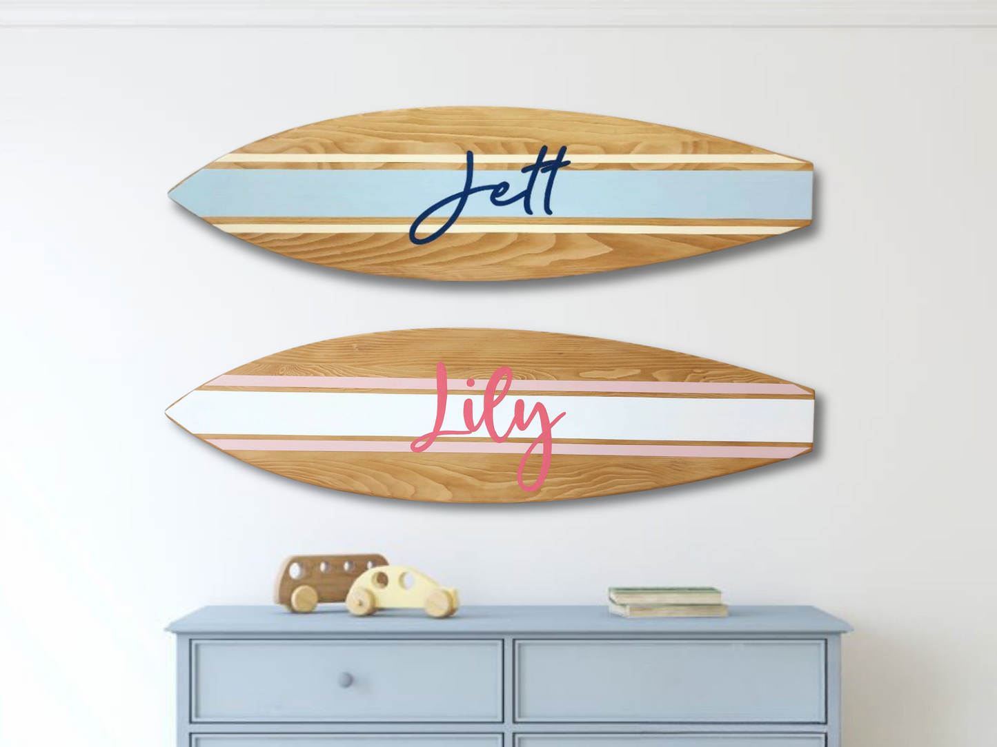 Two wooden surfboard-shaped signs with names 'Jett' and 'Lily' on a white wall above a blue dresser.
