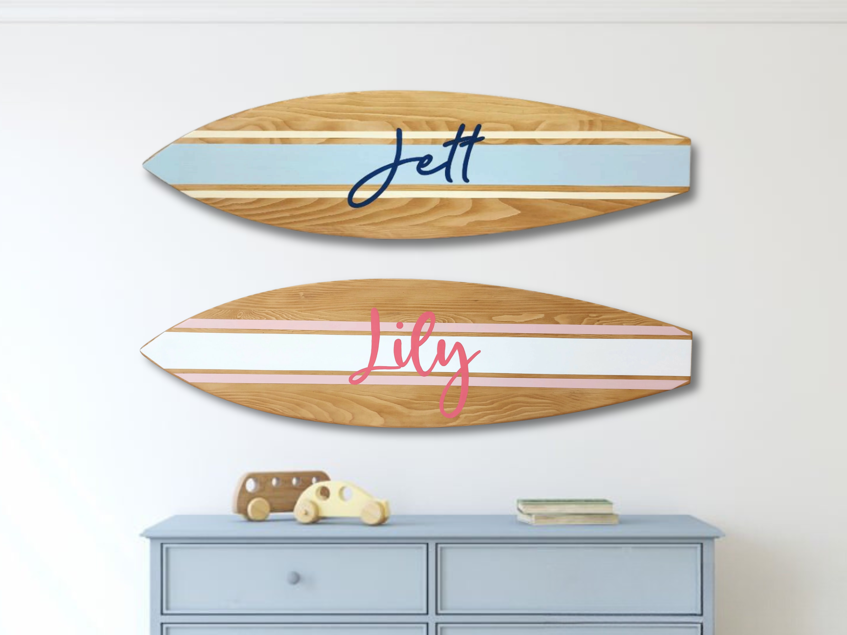Two wooden surfboard-shaped signs with names 'Jett' and 'Lily' on a white wall above a blue dresser.