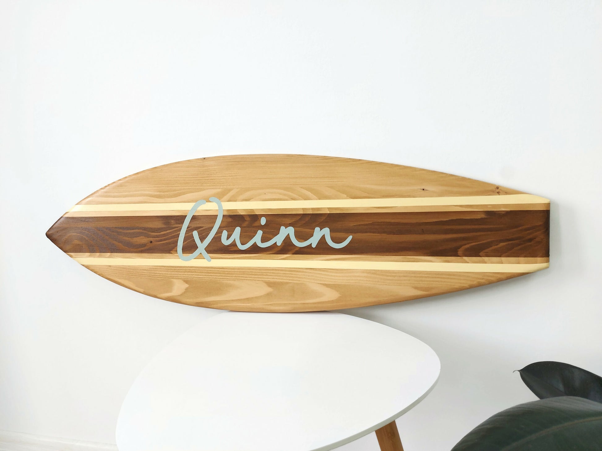 Wooden surfboard-shaped sign with 'Quinn' name on a white wall