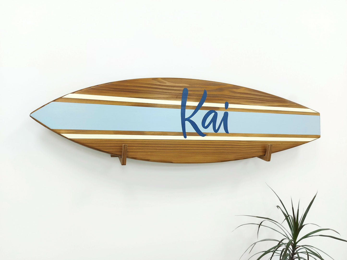 Wooden surfboard-shaped name sign with 'Kai' on a white wall