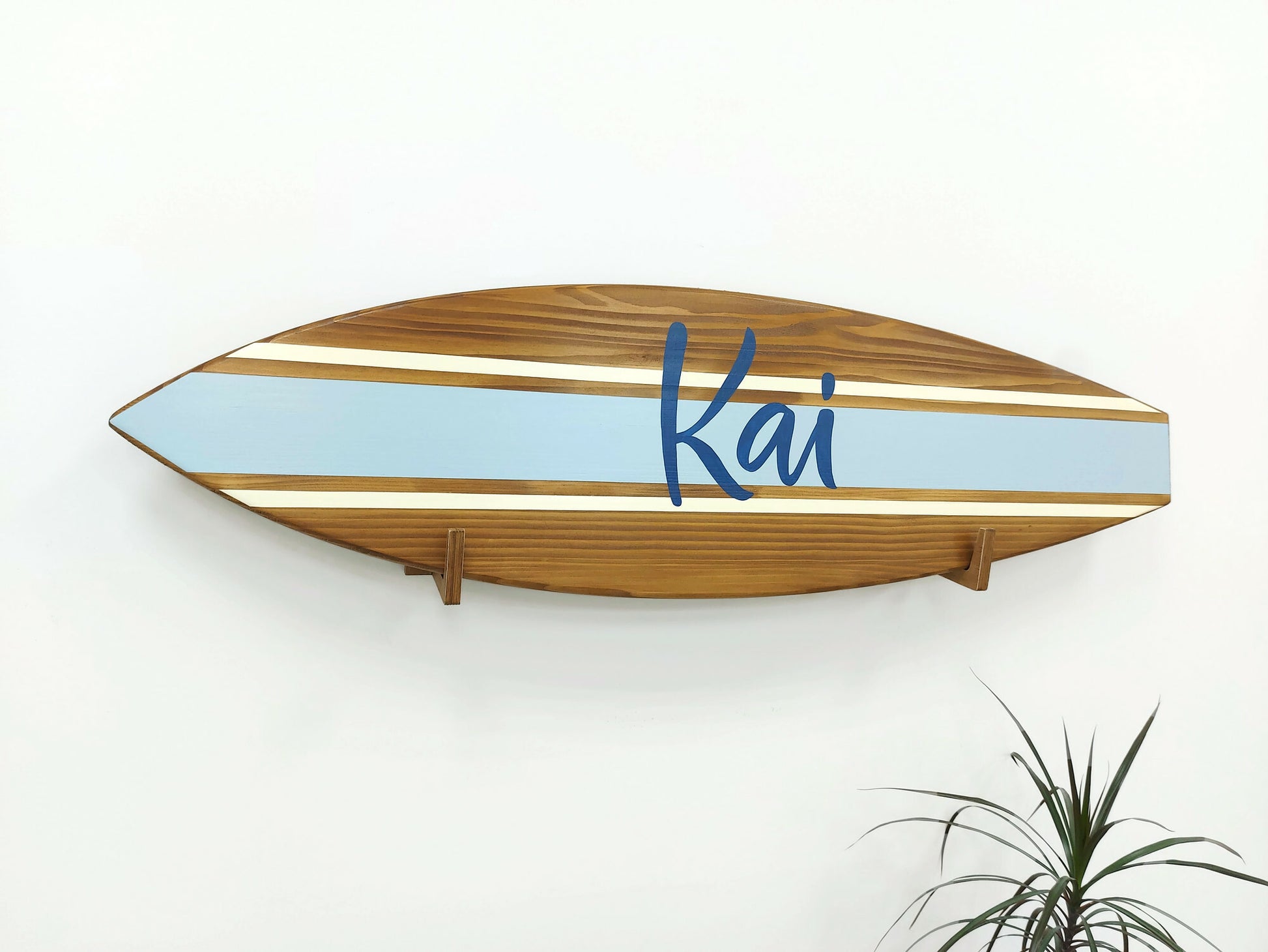 Wooden surfboard-shaped name sign with 'Kai' on a white wall