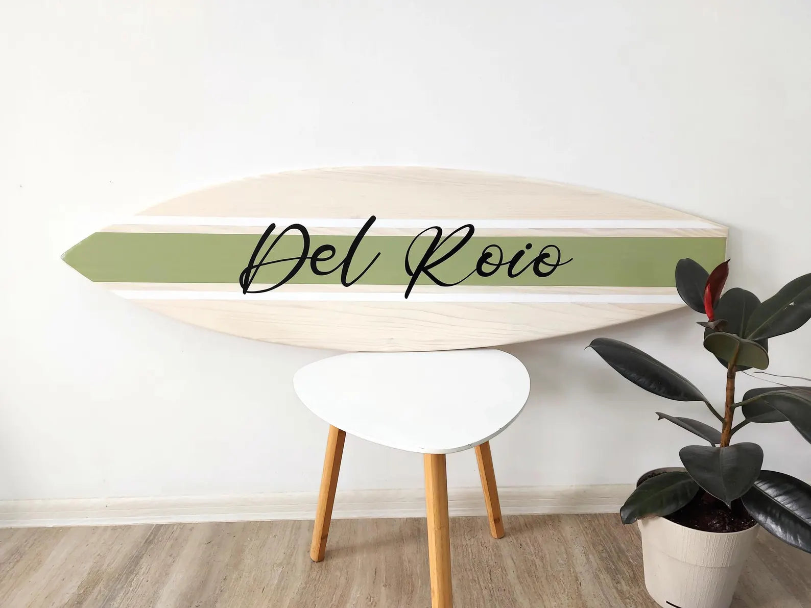 Wooden name sign surfboard with 'Del Roio' branding on a white wall background