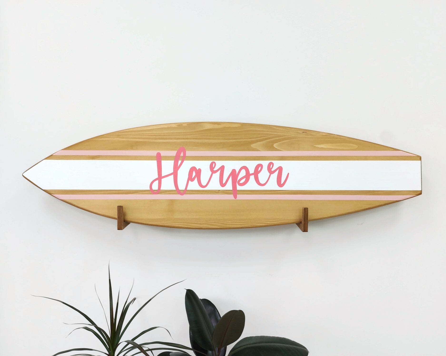 Surfboard-shaped wooden name sign hanging above crib in coastal nursery