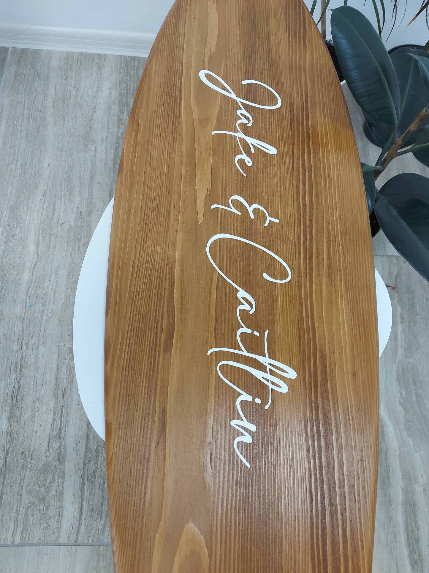 Wooden alternative guest book surboard sign with 'Jake & Caitlin' painted on it, placed indoors.