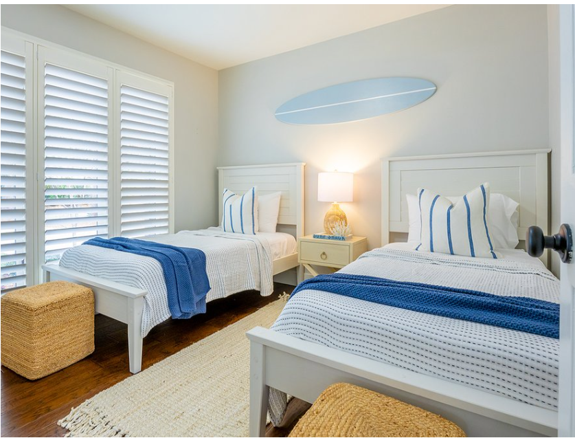 Two twin beds in a bedroom with white bedding and blue surfboard wll si.n