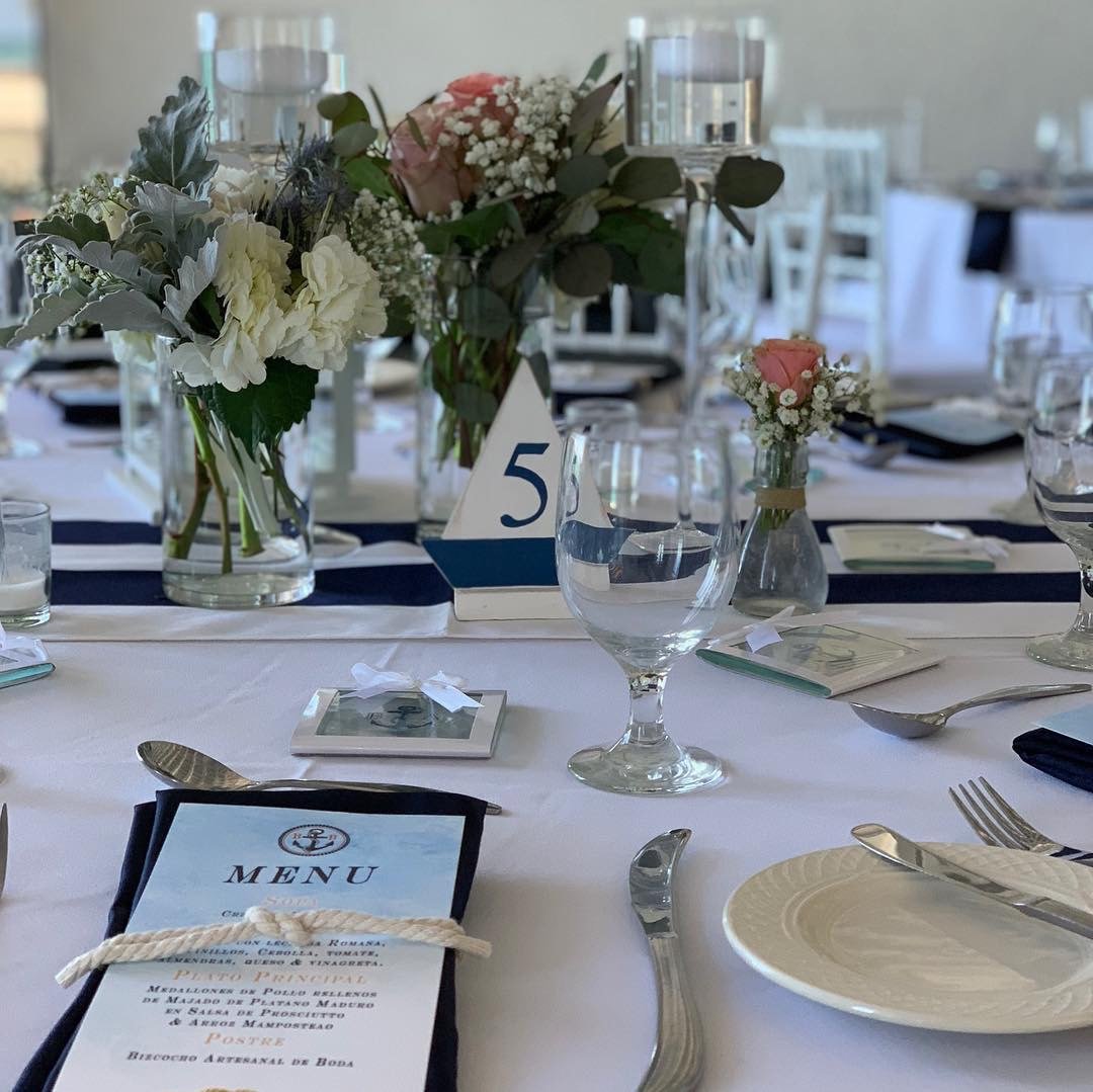 Decorated table setting with flowers, glasses, beach table numbers and a menu on a white tablecloth.