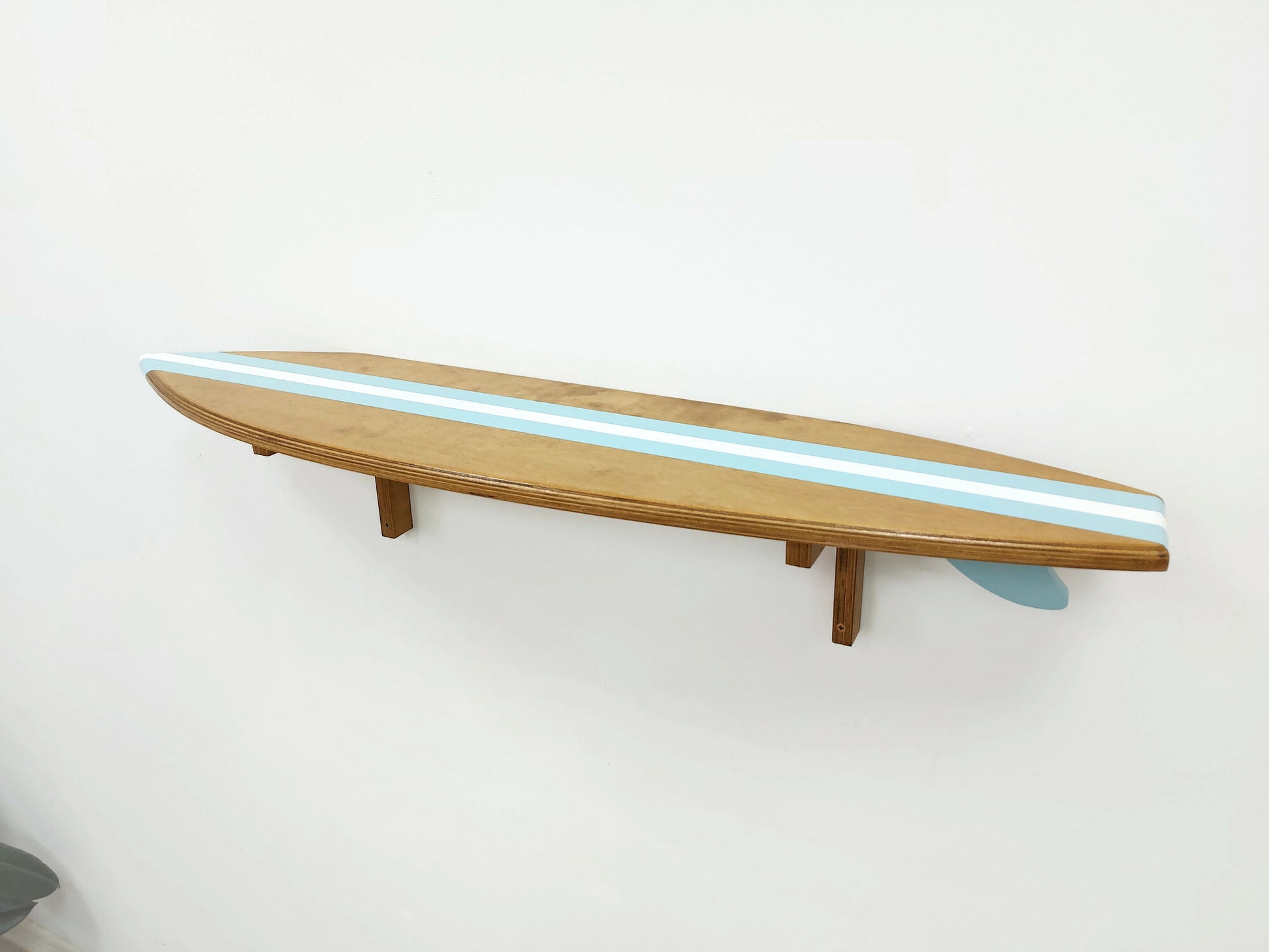 Wooden shelf designed to look like a surfboard with blue stripes on a white wall.