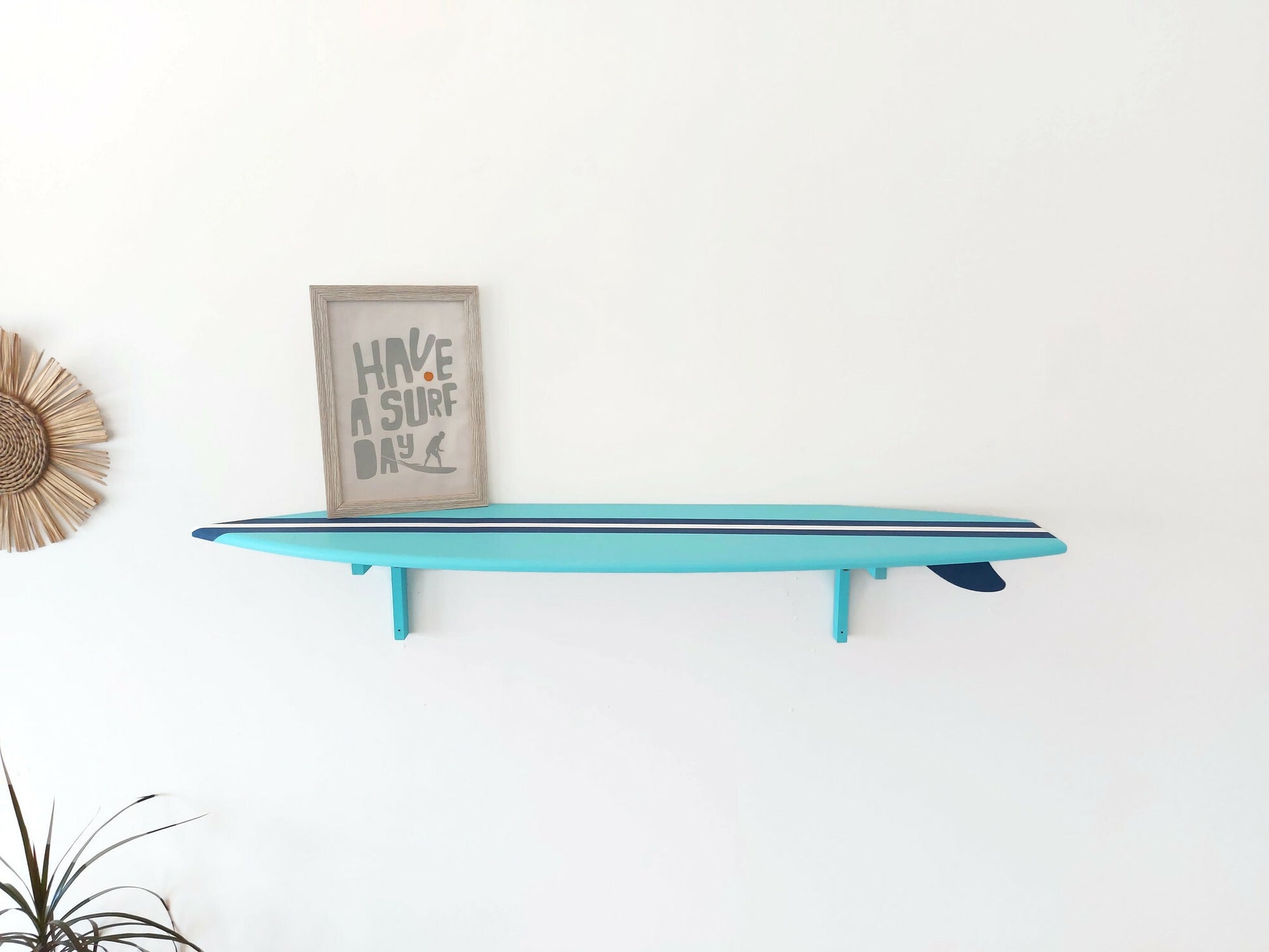 Turquoise surfboard shelf with a framed picture on a white wall