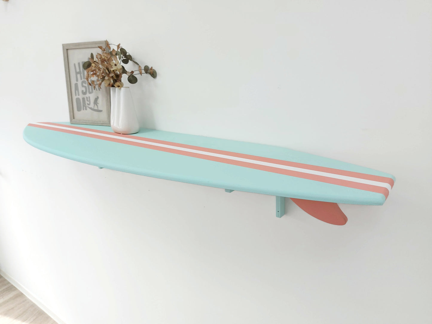 Light blue surfboard-shaped shelf with coral stripes on a white wall.