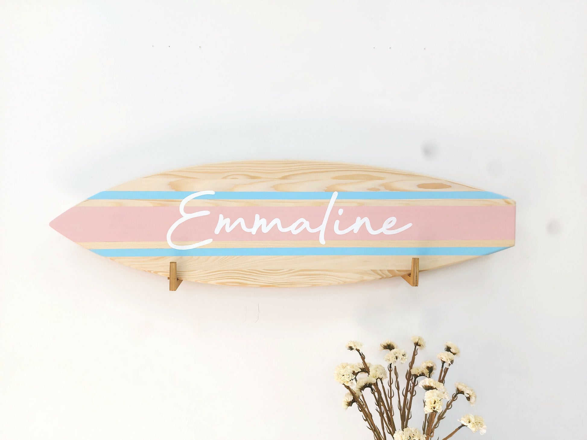 Wooden decorative sign with pink and blue stripes and 'Emmaline' branding on a white background