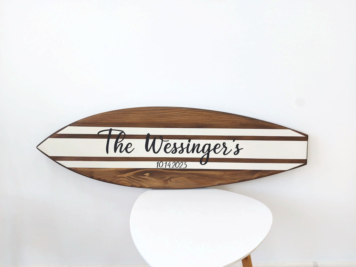 Wooden surfboard-shaped wedding sign with 'The Wessinger's' and date on a white background