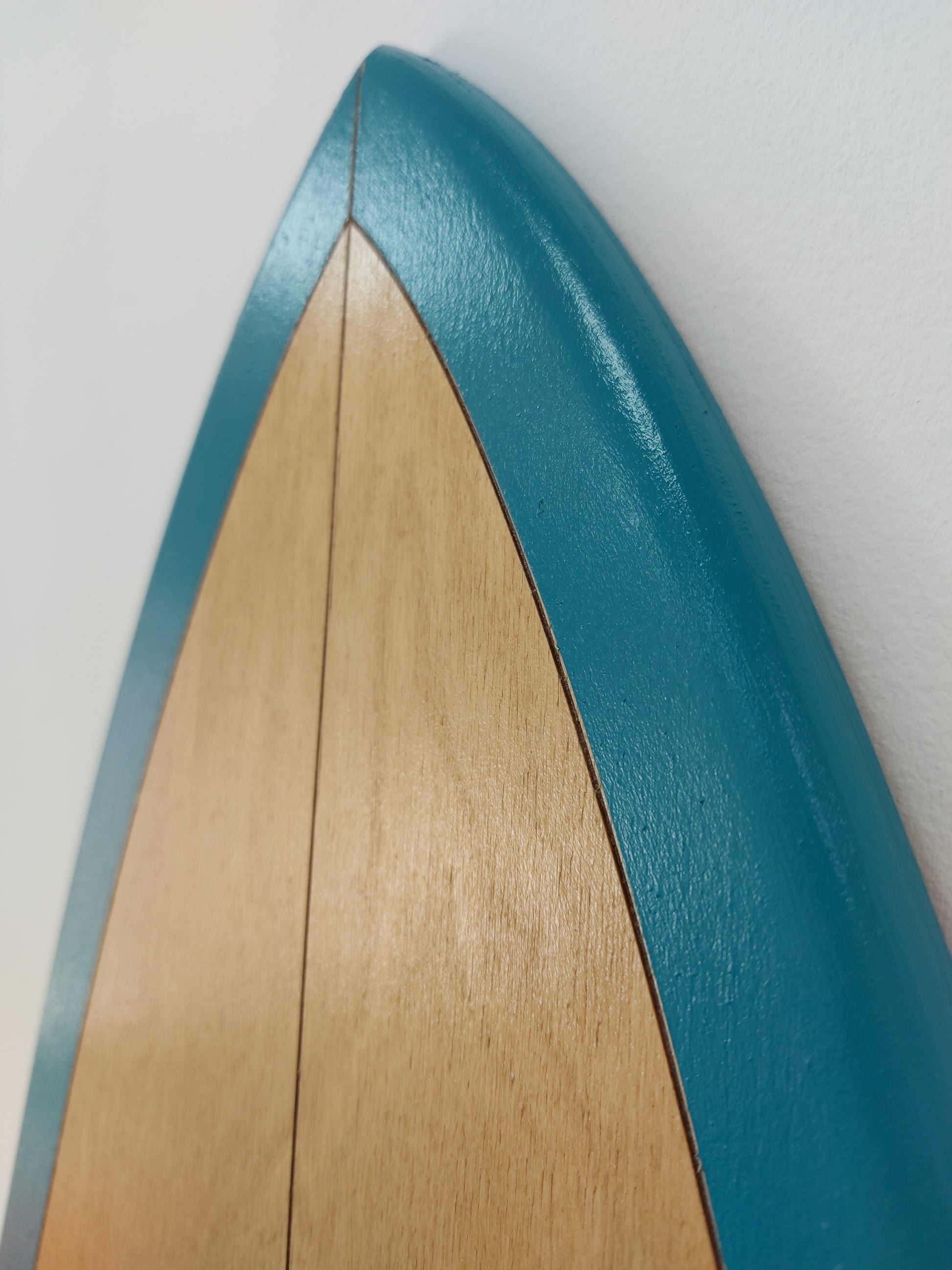 Side view of wooden surfboard decorative wall art with teal border and smooth finish