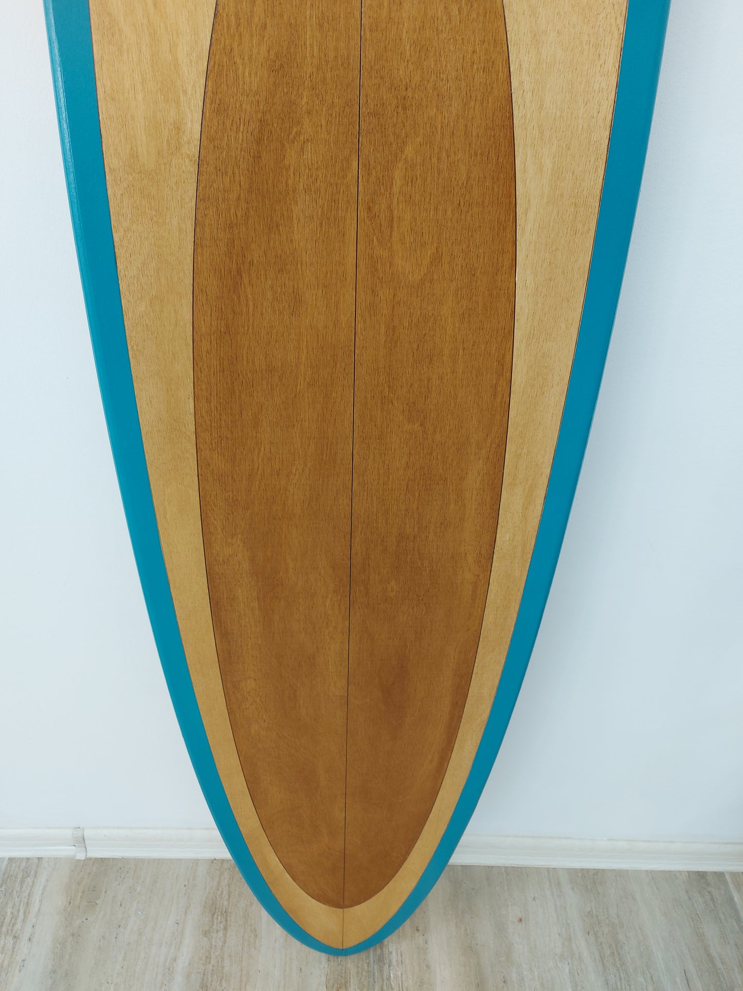 Close-up view of wooden surfboard wall art texture showing natural grain and teal paint edge
